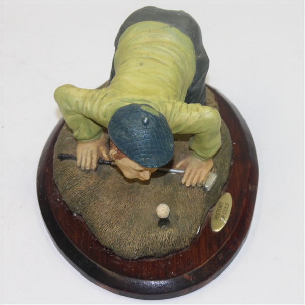 'History of Golf' Figure with Golfer Trying to Blow Ball in Hole